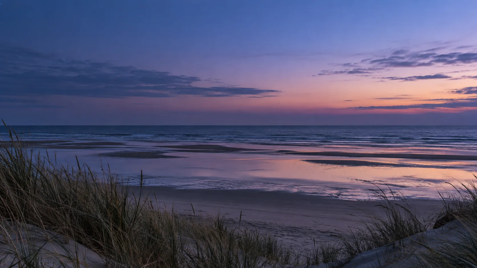 Quiet ocean waves and coastal dunes beneath a soft evening sky