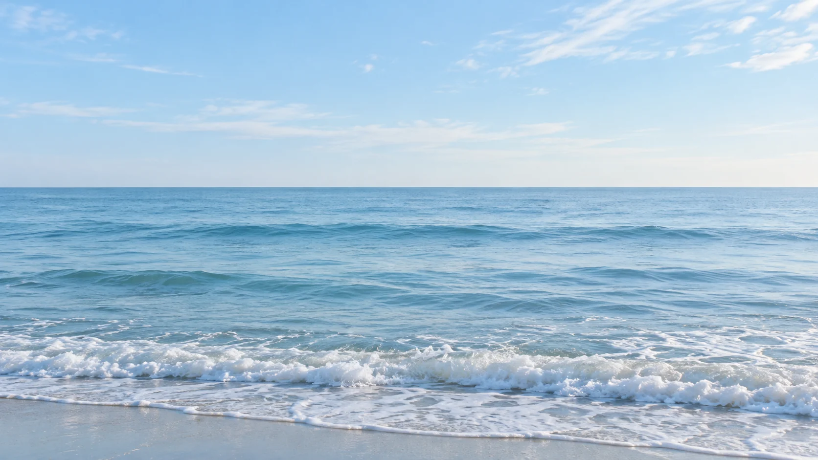 Gentle ocean waves beneath a pale blue morning sky